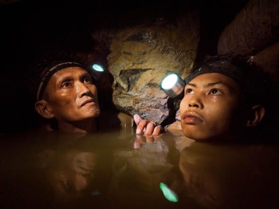 An older miner and a younger boy are chin deep in frigid water 150-meters below the surface as they work a gold mine near Syndicate on the island of Masbate. Image by Larry C. Price. Philippines, 2012.